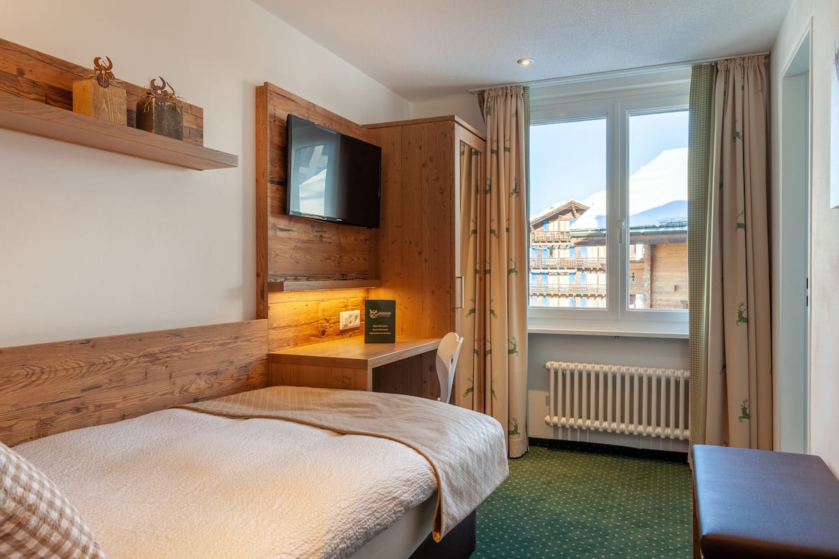 Una habitación de hotel con cama, escritorio, televisor y ventana con cortinas.
