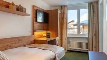 Una habitación de hotel con cama, escritorio, televisor y ventana con cortinas.