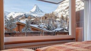 A hotel room with a large window offering a view of snow-covered mountains and a prominent peak.
