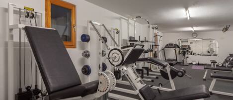A gym with various exercise machines, a window, and a clock on the wall.