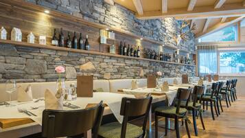 Restaurante com paredes de pedra, vigas de madeira e uma longa mesa de jantar com cadeiras.