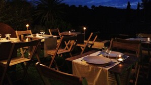 An outdoor dining area with tables and chairs, under a canopy, at dusk. - Les Terrasses de Castelnau (Castelnau-le-Lez)