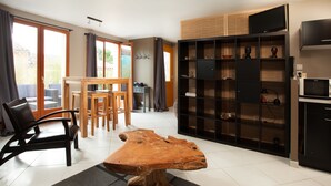 A modern living room with a large wooden coffee table, a dining area with a wooden table and chairs, and a built-in entertainment unit with a TV and shelves. - Les Terrasses de Castelnau (Castelnau-le-Lez)