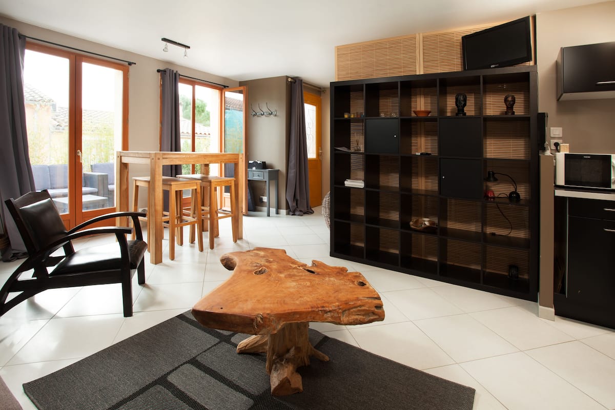 A modern living room with a large wooden coffee table, a dining area with a wooden table and chairs, and a built-in entertainment unit with a TV and shelves.