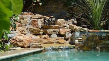 Una piscina al aire libre, una piscina con cascada, sombrillas