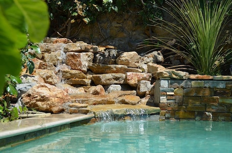 Una piscina al aire libre, una piscina con cascada, sombrillas