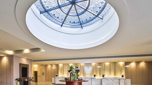 Un vestíbulo de hotel con una recepción central, un tragaluz grande y un suelo de mármol pulido.