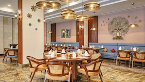 Un restaurante con mesas redondas, sillas de mimbre y lámparas doradas colgantes.