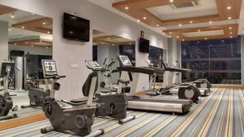 Un gimnasio con cintas de correr, elípticas y bicicletas estáticas, espejos grandes en las paredes y una alfombra estampada.