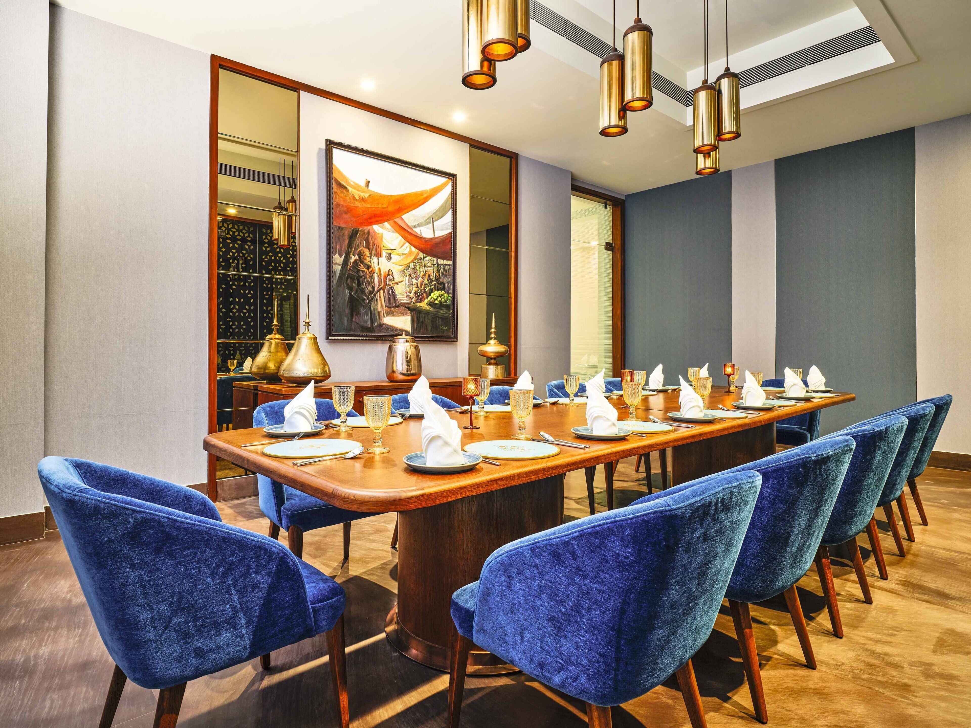 A conference room with a long wooden table, blue upholstered chairs, and a large painting on the wall.