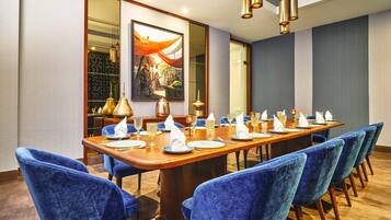 Un salón de conferencias con una larga mesa de madera, sillas tapizadas en azul y un cuadro grande en la pared.