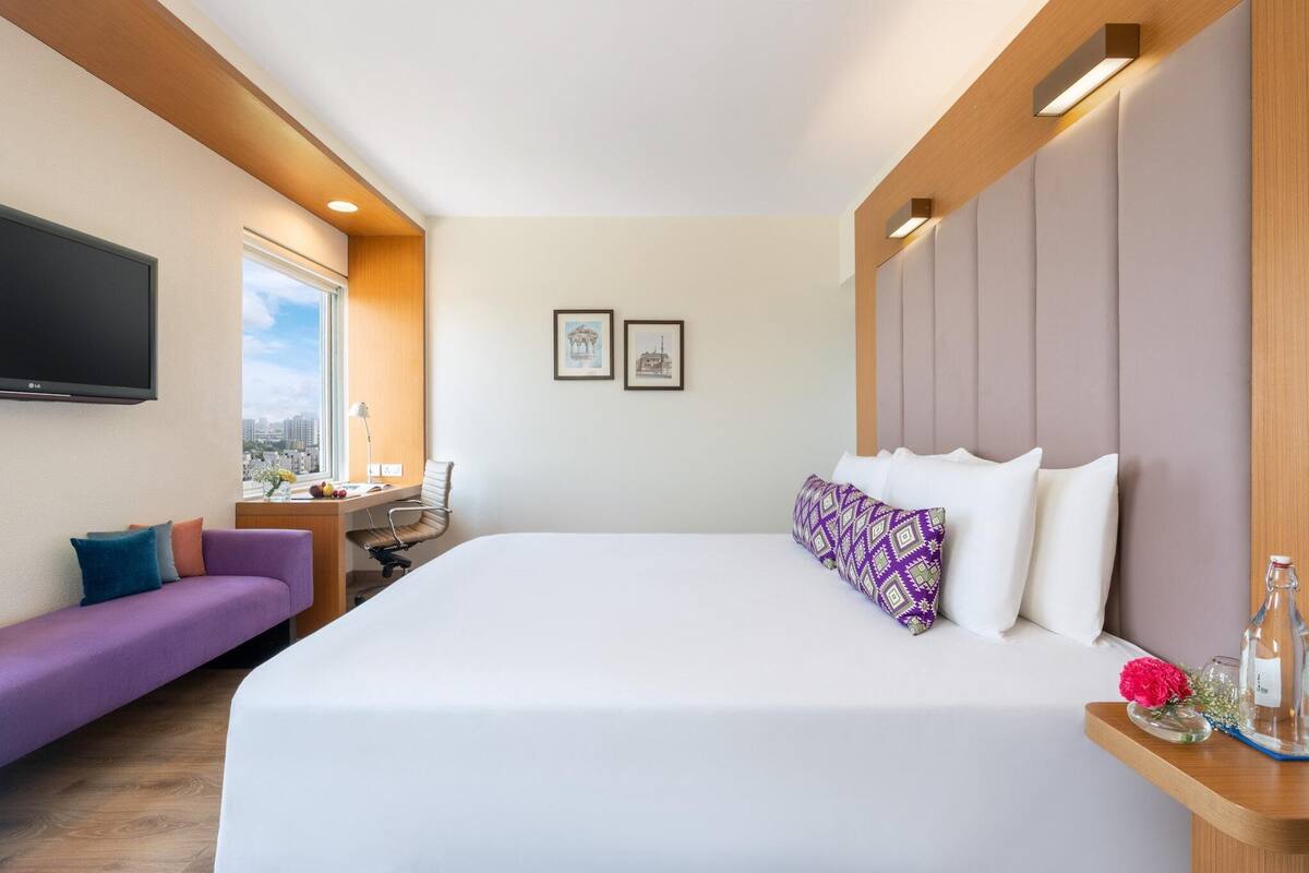 Ein modernes Hotelzimmer mit einem großen Bett, einer Couch, einem Schreibtisch und einem Fernseher.