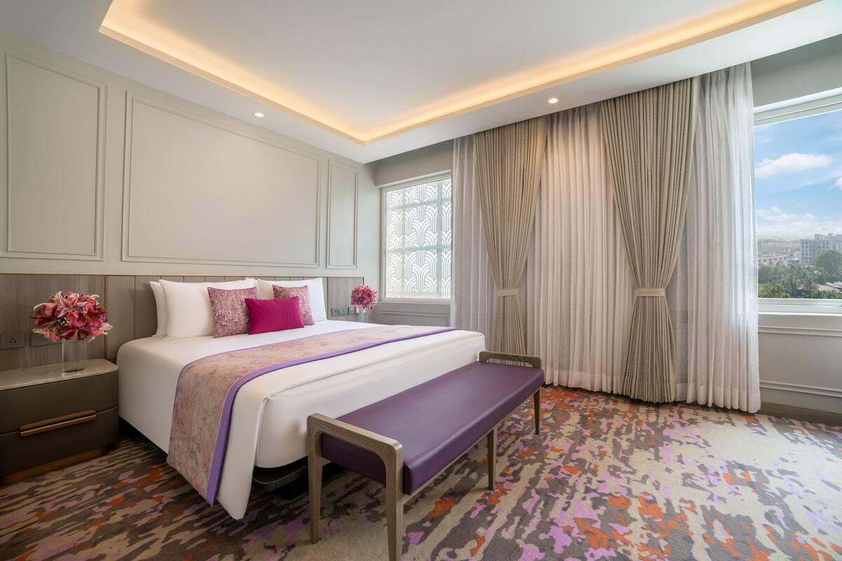 Ein modernes Hotelzimmer mit einem großen Bett, einer Bank, einem Nachttisch und einem Fenster mit Vorhängen.