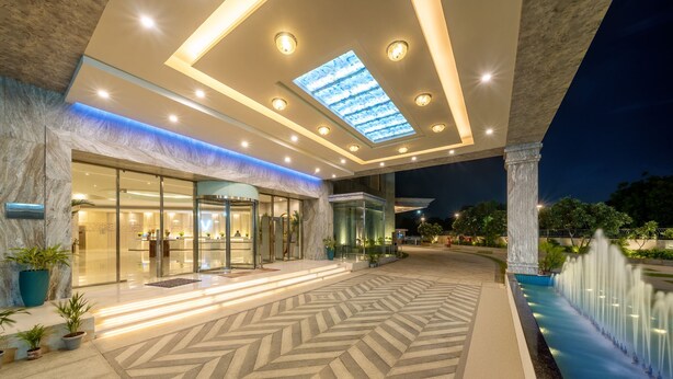Una entrada de hotel moderna con piso de diseño geométrico, fachada de vidrio y fuente de agua.