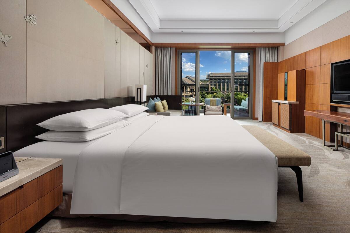 A modern hotel room with a large bed, a flat-screen TV, a desk, and a view of the outdoors.