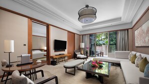 Habitación de hotel moderna con un sofá grande, una mesa de comedor, un televisor y vistas al exterior.