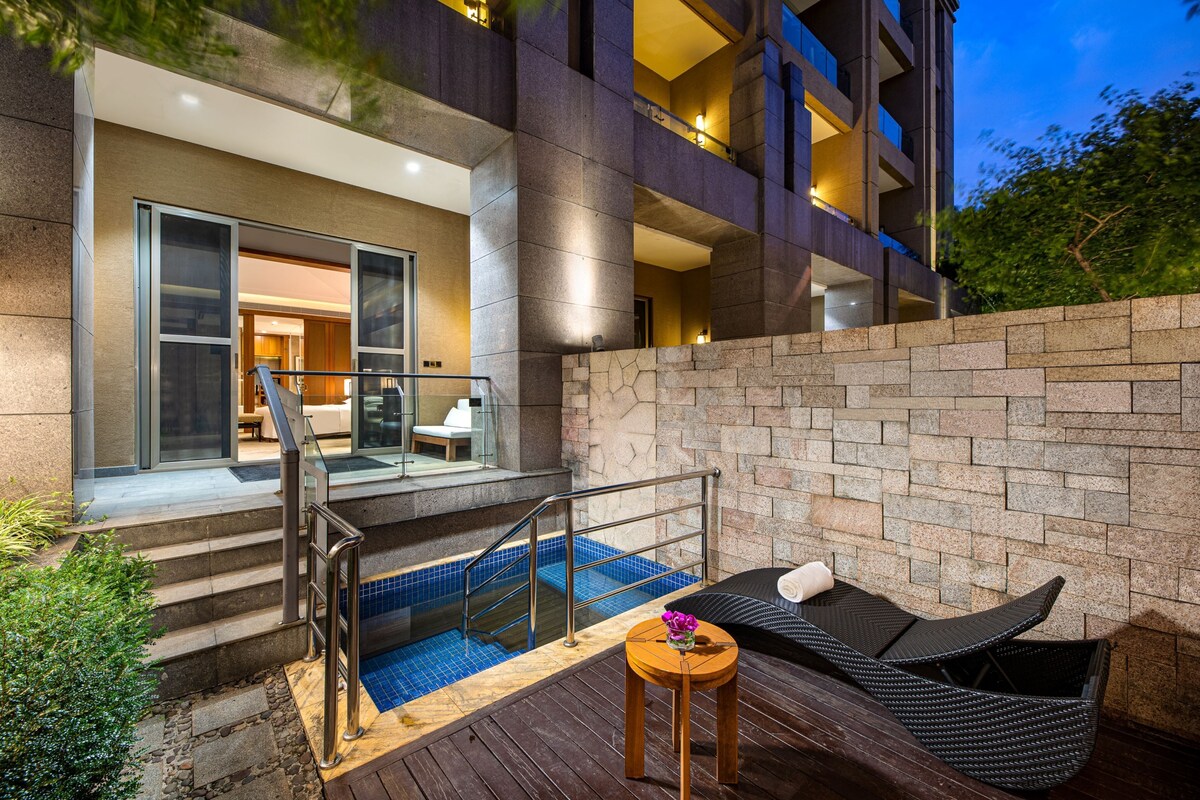 Un edificio moderno con piscina, mobiliario exterior y una escalera que lleva a la entrada.