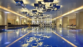 Una amplia piscina interior con vistas despejadas al techo y las paredes, que destaca por un diseño moderno con lámparas geométricas y una zona de estar central.