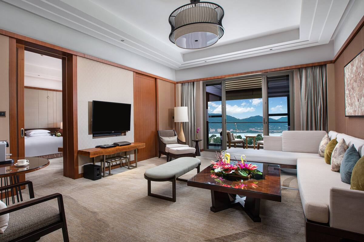 A hotel room with a bed, a TV, a sofa, a coffee table, and a view of the sea.
