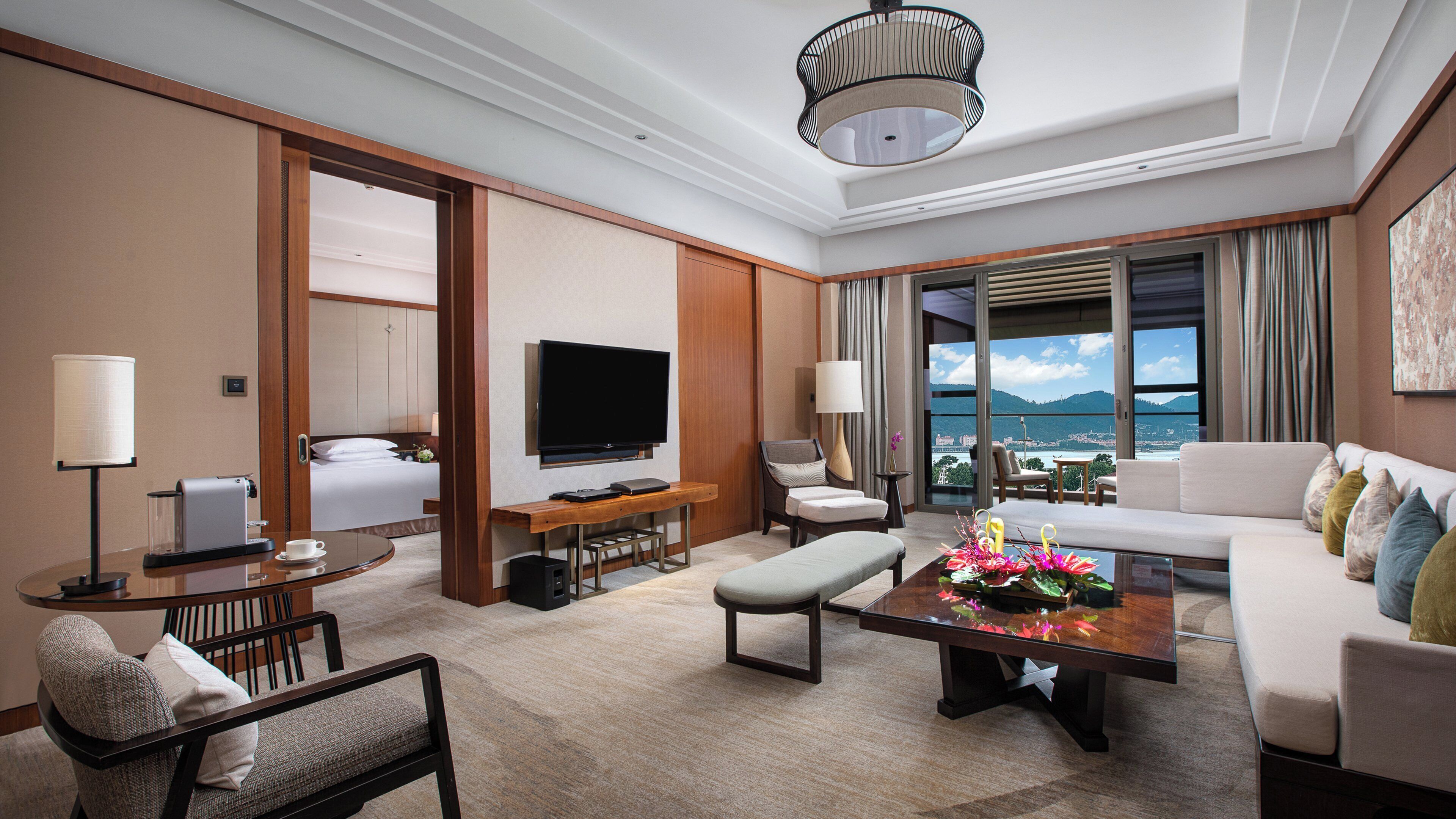 A hotel room with a bed, a television, a sofa, a coffee table, and a view of the outdoors.