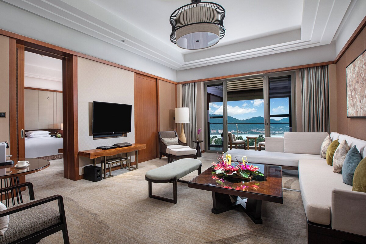 Habitación de hotel con cama, televisor, sofá, mesa de centro y vista al mar.