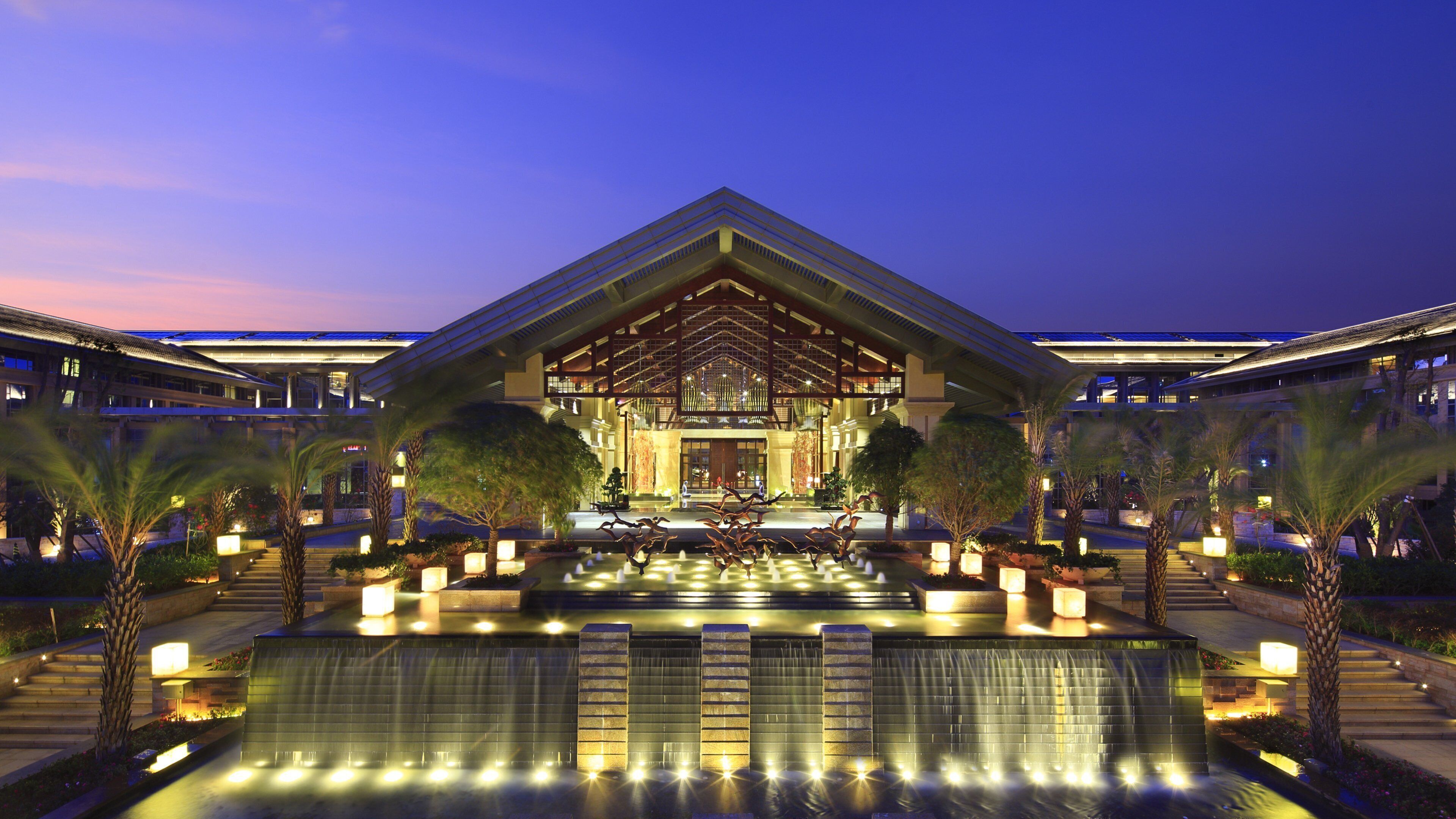 A modern hotel with a central atrium, a water feature in front, and symmetrical landscaping.