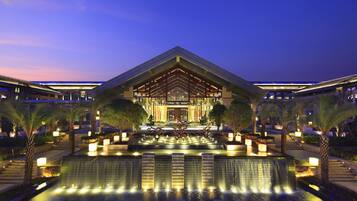 A modern hotel with a central atrium, a water feature in front, and symmetrical landscaping.