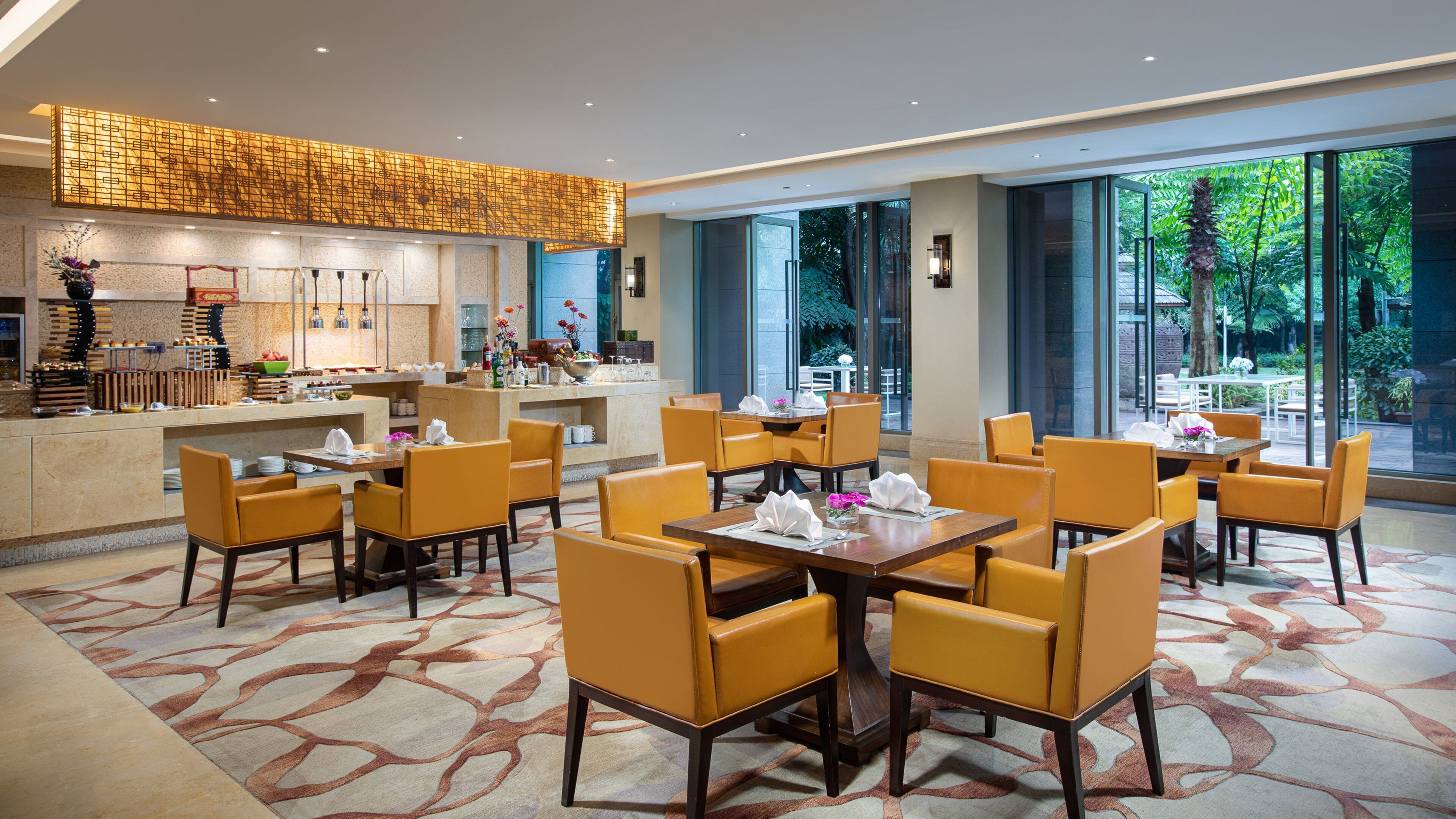 A hotel lobby with a reception area, dining tables with chairs, and large windows offering a view of the outdoors.