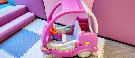 Um carro de brinquedo rosa sobre um piso estampado.