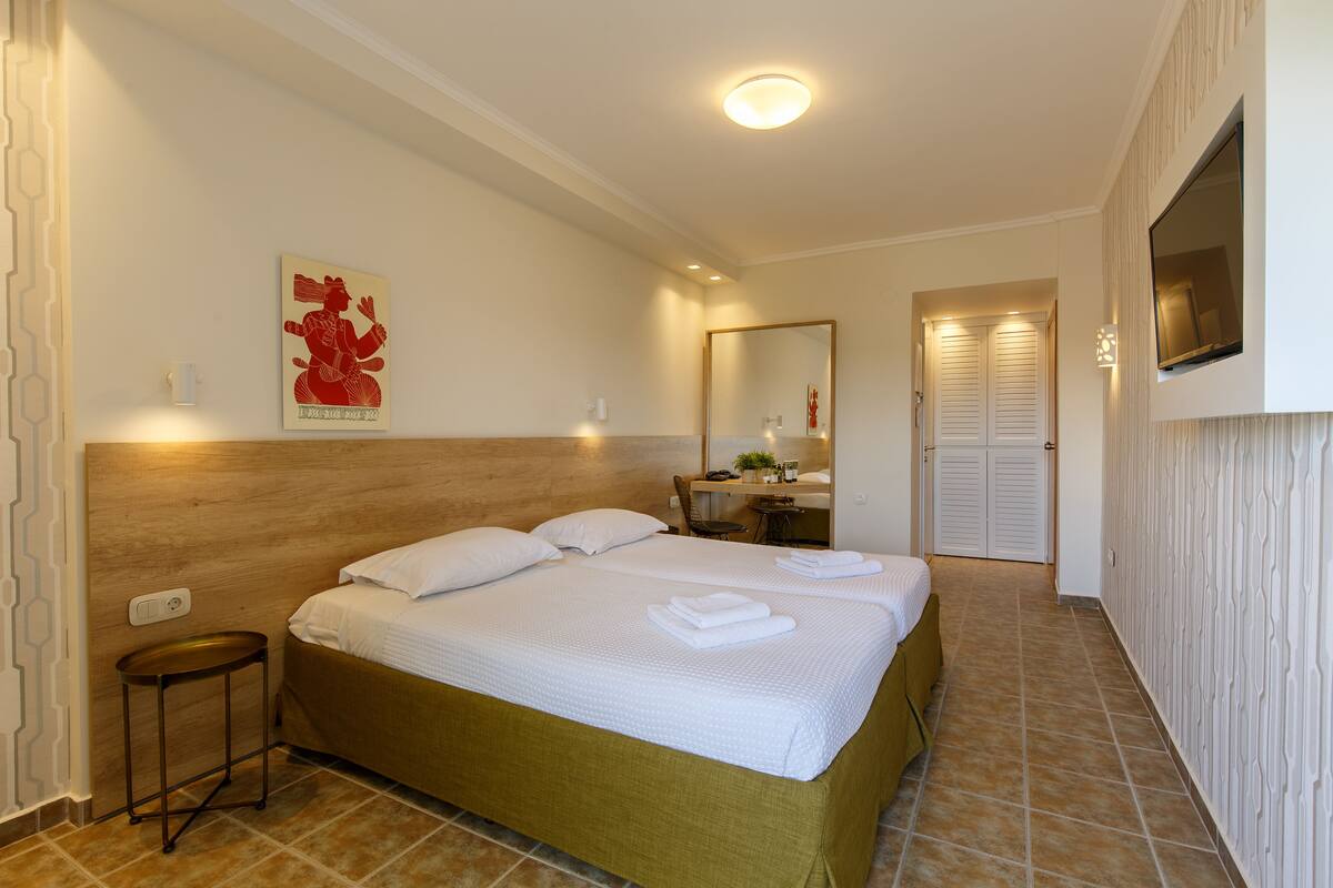 A hotel room with a large bed, a small table, a mirror, and a TV mounted on the wall.