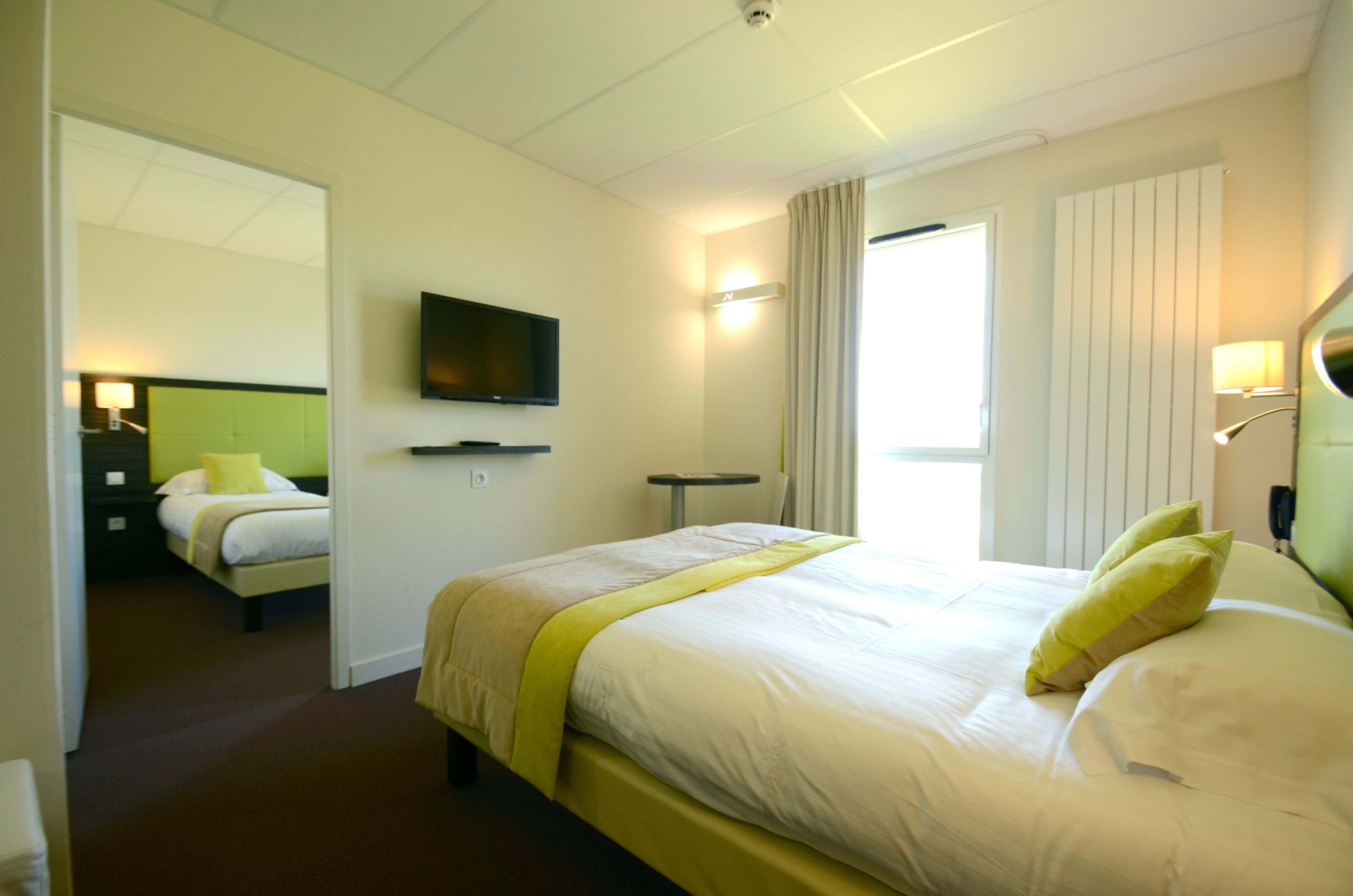 A hotel room with a bed, a television, a bedside table, and a window with curtains.