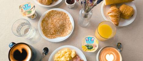 A breakfast table with croissants, scrambled eggs, sausages, coffee, and juice.