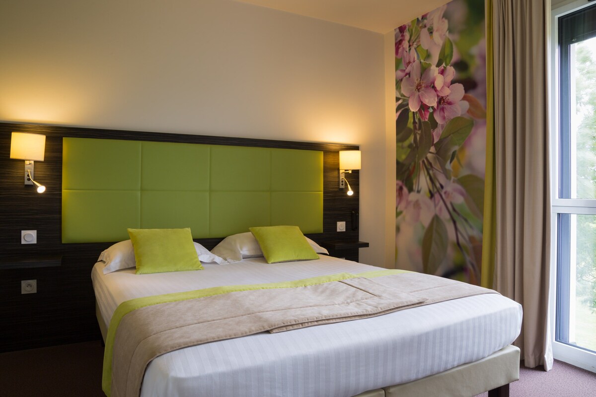 A hotel room with a large bed, two bedside lamps, a green headboard, and a floral wall mural.