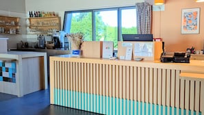 Ein Empfangsschalter mit Blick auf Bäume, eine Kaffeemaschine und eine Theke mit verschiedenen Artikeln.