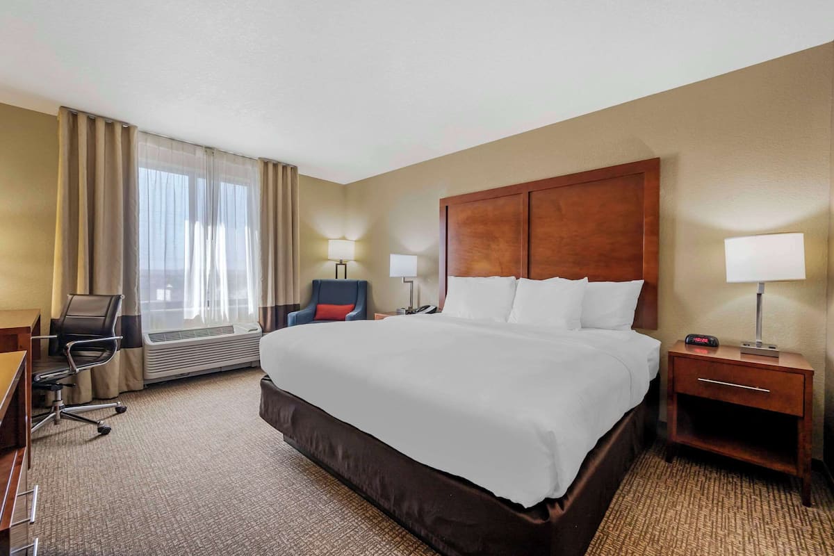 A hotel room with a large bed, a desk, a chair, and a window with curtains.