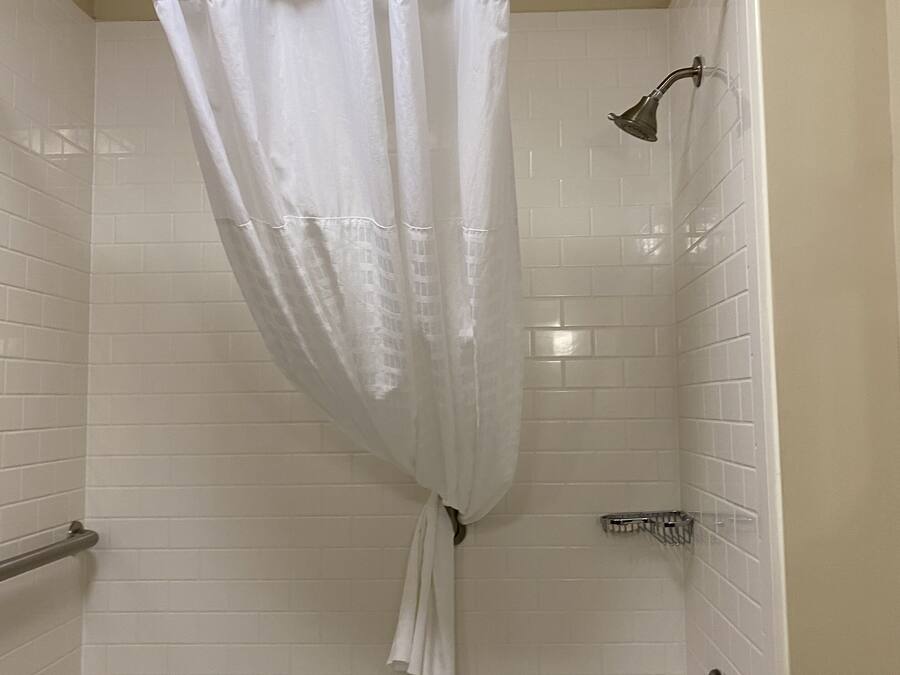 Un baño con paredes de azulejos blancos, una bañera, una ducha con cabezal de ducha y un inodoro.
