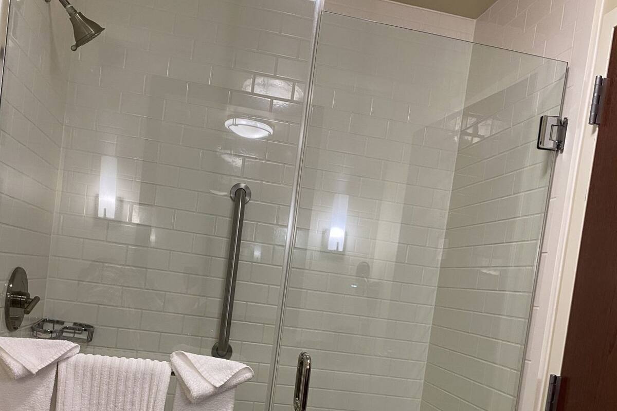 A glass-enclosed shower stall with a handheld showerhead, a glass door, and a towel rack with three towels.
