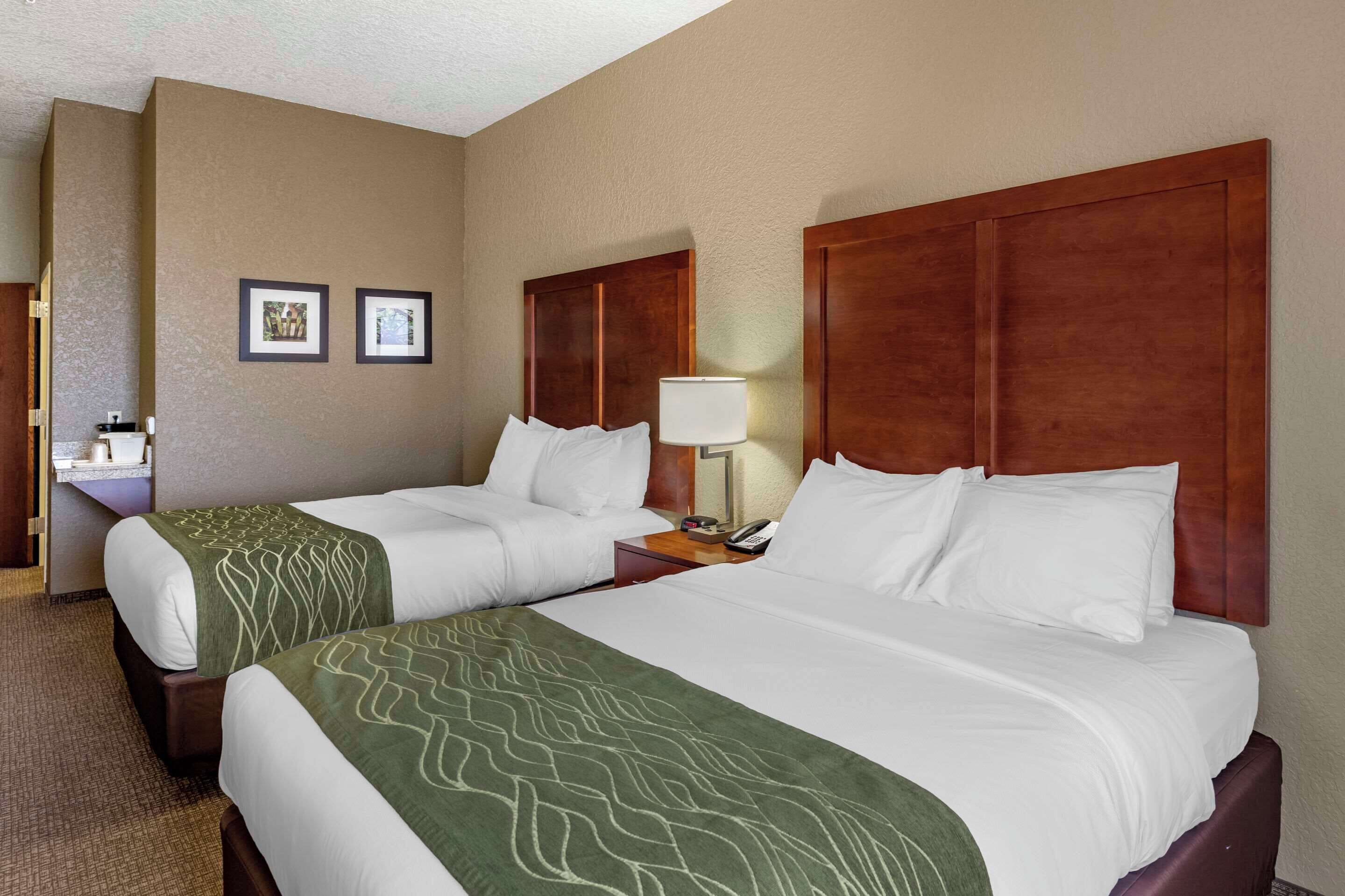 A hotel room with two beds, a nightstand with a lamp, and a small table with a phone.