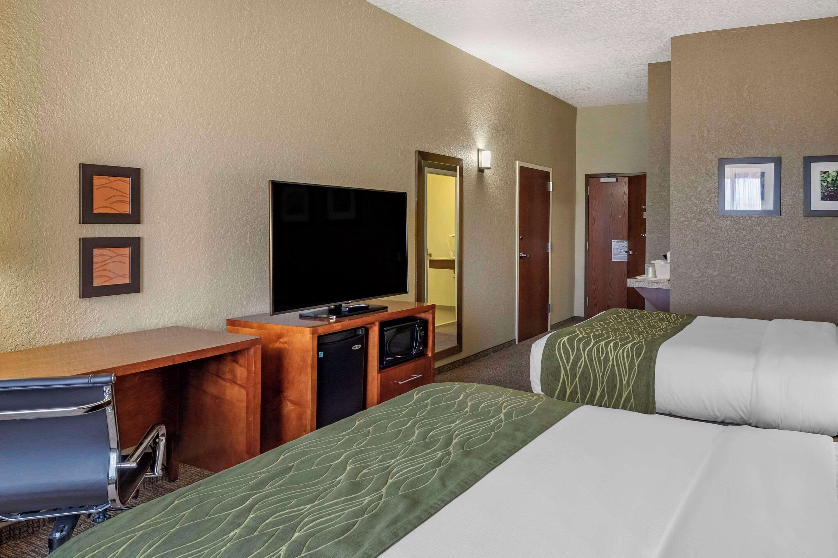 A hotel room with two beds, a desk with a television, and a small kitchenette.