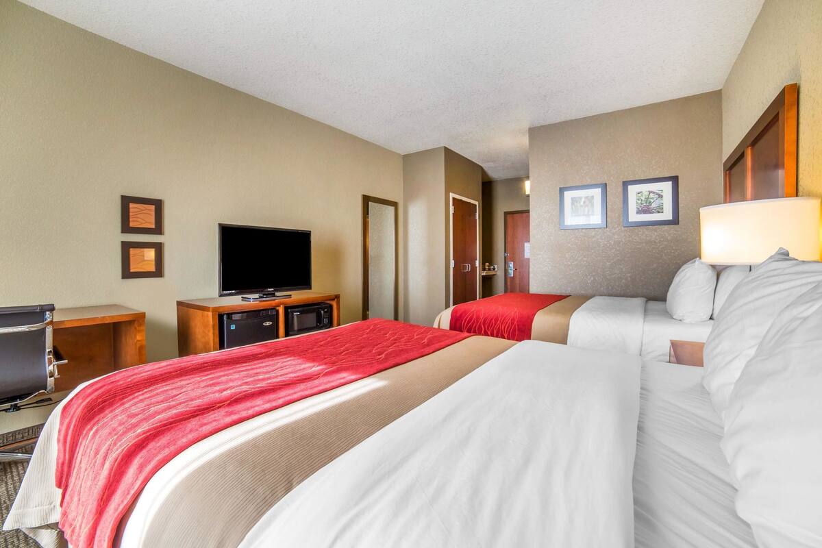 A hotel room with two beds, a TV, a desk, and a microwave.