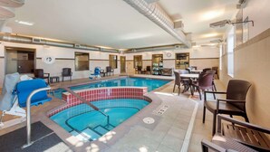 An indoor swimming pool with a tiled edge, surrounded by seating areas and a covered patio.