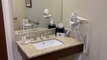 A bathroom with a granite countertop sink, a hairdryer, a mirror, and a trash bin.