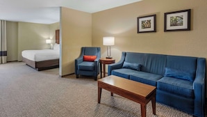 A hotel room with a bed, a blue armchair, a blue sofa, a wooden coffee table, and two framed pictures on the wall.