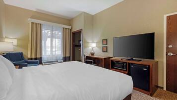 A hotel room with a large bed, a desk with a flat-screen TV, a microwave, and a mini-fridge.