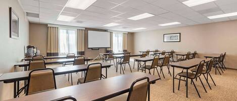 A conference room with multiple tables and chairs, a projector screen, and a large window with curtains.