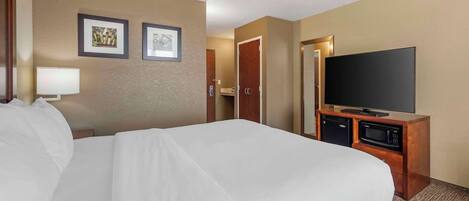 Une chambre d’hôtel avec un grand lit, un téléviseur à écran plat, un four à micro-ondes et un petit bureau avec une lampe.