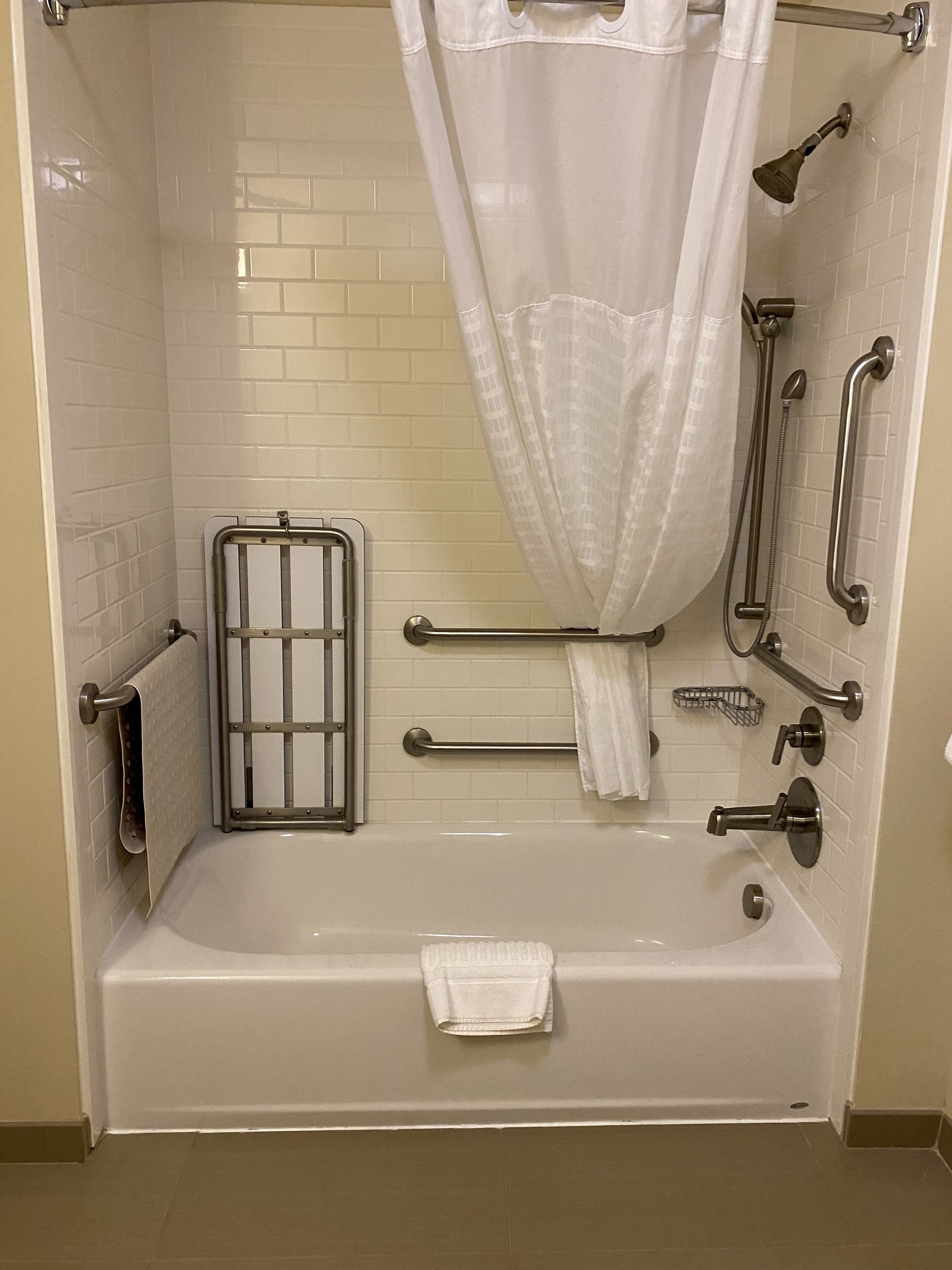 A modern bathroom with a walk-in shower, grab bars, a handheld showerhead, and a white tiled wall.