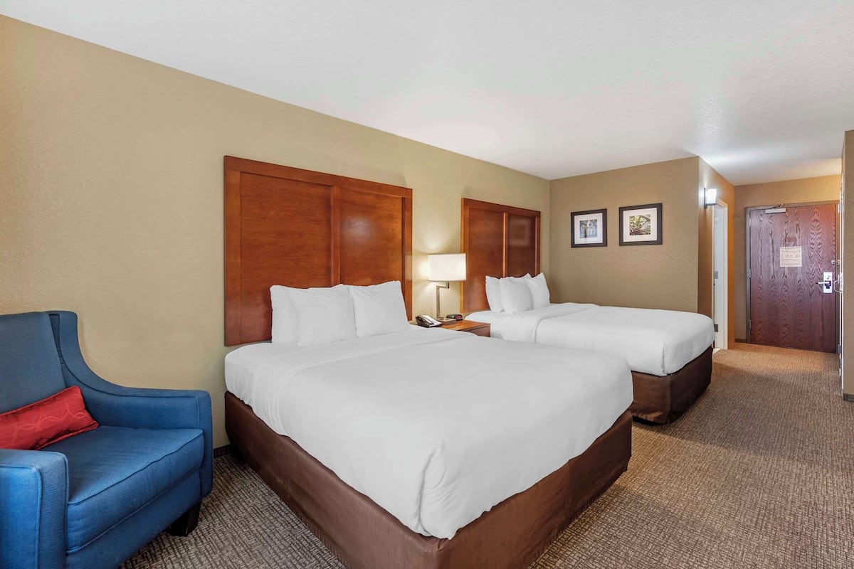 A hotel room with two beds, a blue armchair, a lamp, and a door with a sign.