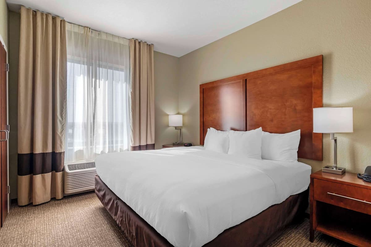 A hotel room with a large bed, two bedside tables, a nightstand, a lamp, and a window with curtains.