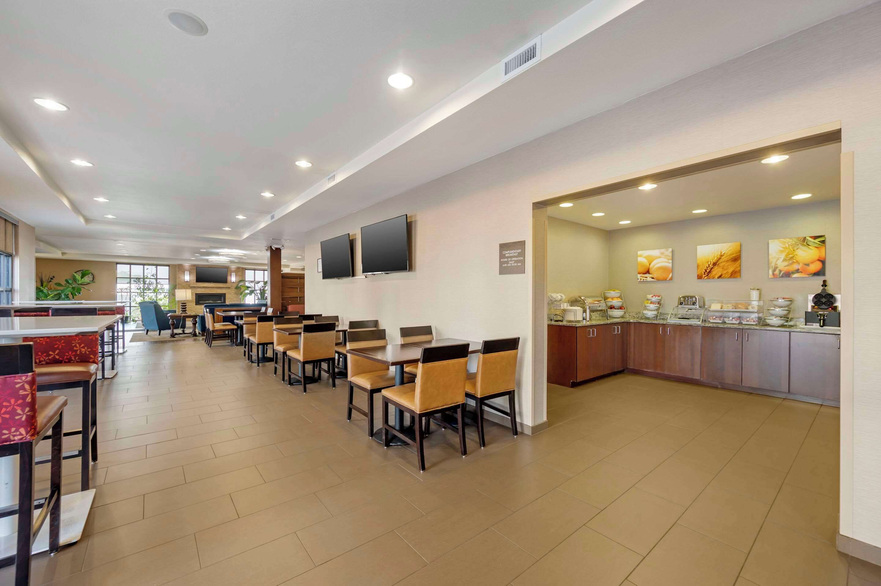 A spacious restaurant with multiple dining tables and chairs, a kitchen area with a buffet, and a large window providing natural light.